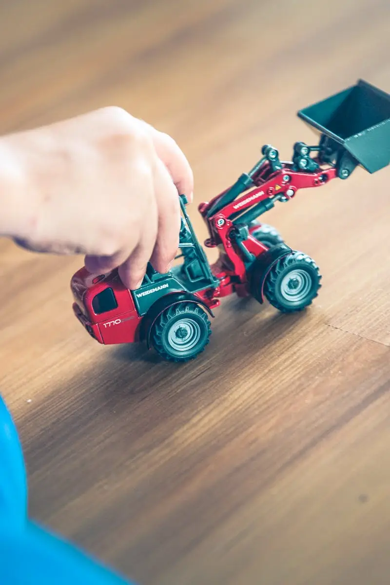 A child plays with a toy excavator on a wooden floor, enjoying creative indoor playtime.